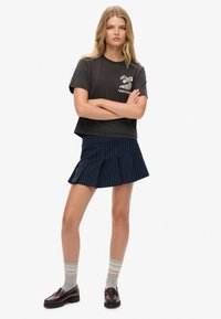 Camiseta negra recortada con diseño "NOTE FRESH", combinada con una falda plisada de rayas azul marino. Llevada con calcetines rayados grises y mocasines negros.