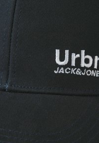 Casquette en coton noir avec une visière courbée, ornée du texte de logo brodé blanc "Urban JACK & JONES" et de détails de couture visibles.