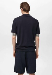 Polo shirt a righe blu navy con maniche corte, dotato di colletto classico e vestibilità rilassata, abbinato a pantaloni corti scuri per un look coordinato.