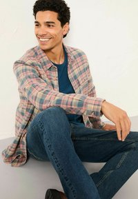 Karierte Flanellhemd in Pastellfarben, blaues T-Shirt und dunkle Jeans. Sitzende Pose mit strukturiertem Stoff und lässigen Designdetails.