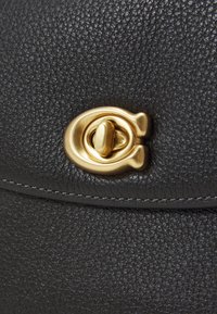 Svart texturerad läderhandväska med ett guld cirkulärt lås. Avslutad med kontrasterande vit sömnad för extra detalj.