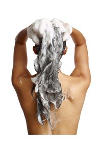 Capelli neri con schiuma bianca vengono insaponati, visti da dietro, mostrando una texture bagnata e la pelle sulle spalle.