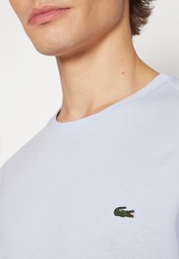 Gros plan sur une personne portant une chemise bleu clair avec un petit logo crocodile vert sur la poitrine.