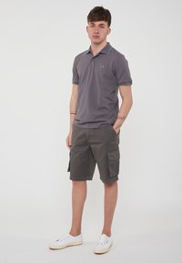 Polo grigio con dettagli turchesi abbinato a pantaloni cargo grigi fino al ginocchio e sneakers bianche. Design semplice con maniche corte.