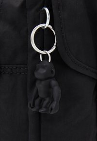 Black monkey-shaped keychain attached to a silver keyring, set against a textured black fabric background.