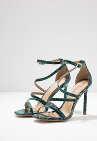 Tummansininen käärmeennahkapainatus korkeat sandaalit, joissa on useita ristikkäisiä hihnoja ja avoimet varpaat; varustettu ohuella stiletto-korkolla ja liukkaalla sisäpohjalla.