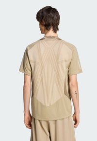 Tělové sportovní tričko s krátkými rukávy, s geometrickým vzorem na zádech a hladkou texturou. Lze doplnit o odpovídající světle zbarvené šortky.