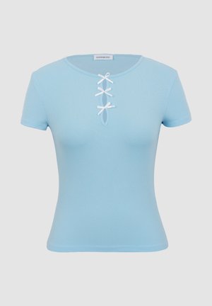 Haut bleu clair côtelé à manches courtes avec encolure ronde et trois petits nœuds blancs alignés verticalement le long d'une fente au niveau de la poitrine.