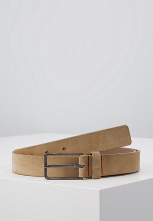 Světlohnědý semišový pásek s obdélnou tmavou kovovou přezkou, položený na bílé ploše se šedým pozadím.