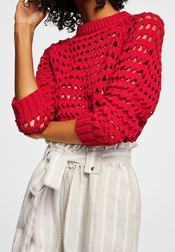 Pull rouge en tricot avec un motif texturé ajouré, longueur courte et encolure arrondie. Associé à un pantalon rayé clair taille haute.