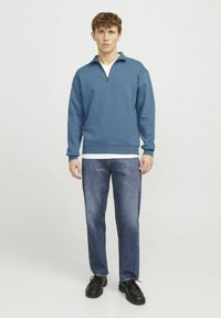 Blue fleece pullover with a half-zip collar, long sleeves, and ribbed cuffs, paired with blue jeans and black lace-up shoes.