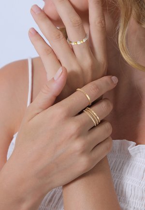 Gouden en parellen ringen aan vingers; één heeft gladde gouden banden, een andere heeft getextureerde accenten, en één toont kleine gouden kralen te midden van geëtste kralen.