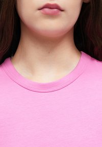 Różowa bawełniana koszulka z okrągłym dekoltem, charakteryzująca się gładką fakturą i starannym wykończeniem wokół kołnierza.