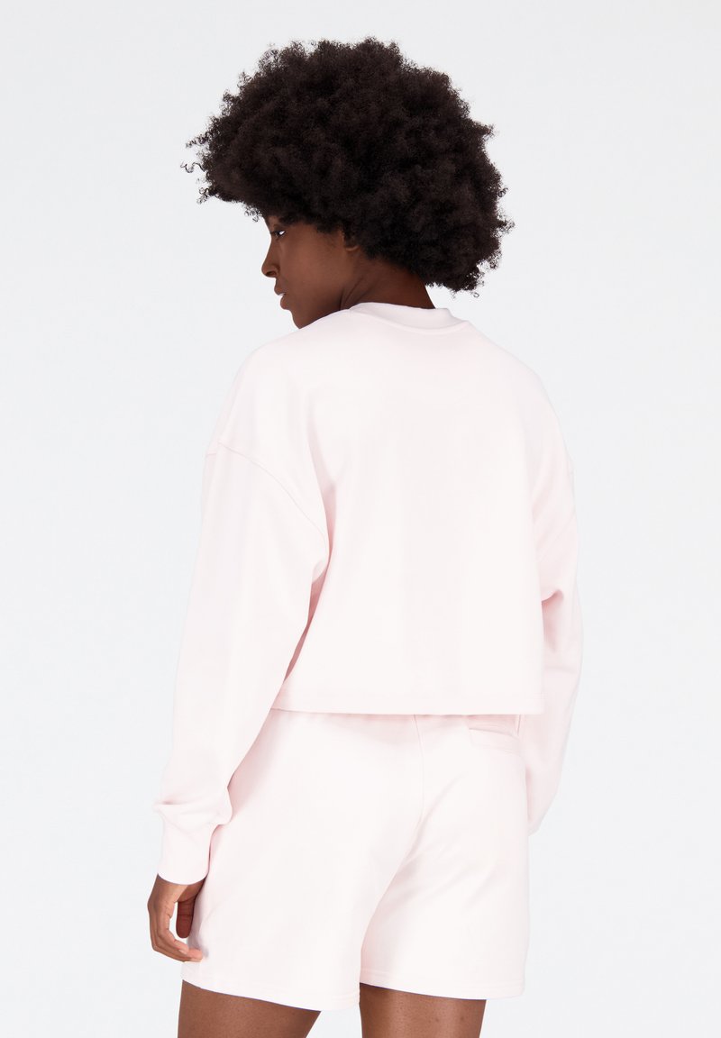 Sudadera corta rosa claro con mangas largas, puños acanalados y un corte relajado, combinada con pantalones cortos a juego de un color similar.
