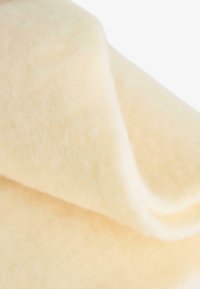 Tessuto morbido di colore crema con una texture liscia, caratterizzato da un bordo piegato che evidenzia il suo aspetto delicato e soffice.