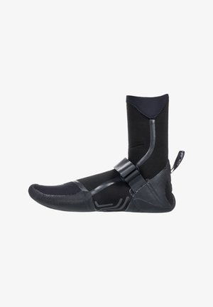 Black neoprene water boot with reinforced toe, adjustable strap, textured sole, and ankle height for added support and protection.