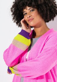 Helles pinkes Strickjacke mit kontrastierenden mehrfarbigen gestreiften Bündchen in Lila, Gelb und Beige. Stricktextur, offenes Vorderdesign.