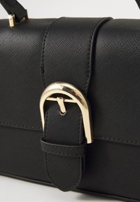 Sac à main noir texturé avec un détail en boucle dorée, au design structuré, doté d'une poignée et d'une bandoulière réglable.