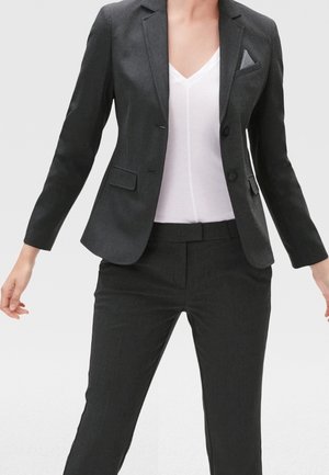 Blazer ajusté gris foncé à deux boutons, avec des revers en pointe et une poche poitrine. Assorti avec un pantalon ajusté coordonné et un haut blanc à col en V.