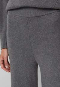 Close-up of a person wearing grey knit pants and a matching sweater, showing texture and ribbed waistband and cuffs.