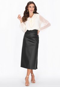 Musta satiinihame, jossa edessä halkio, yhdistetty kermaiseen puseroon, jossa on röyhelöinen pääntie ja läpikuultavat pitkät hihat. Hopeiset remmisandaalit.