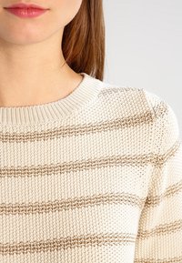 Maglione lavorato a maglia con base crema e strisce orizzontali marroni, caratterizzato da un colletto a coste e un tessuto testurizzato.