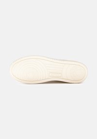 Sole di sneaker di colore crema con gomma testurizzata. Presenta motivi circolari e lineari, incisione del logo e un tallone arrotondato.