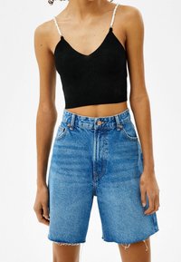 Svart ribbat crop top med justerbara vita pärlremmar, parat med högmidjade blå denimshorts med fransad nederkant och ljus tvätt.