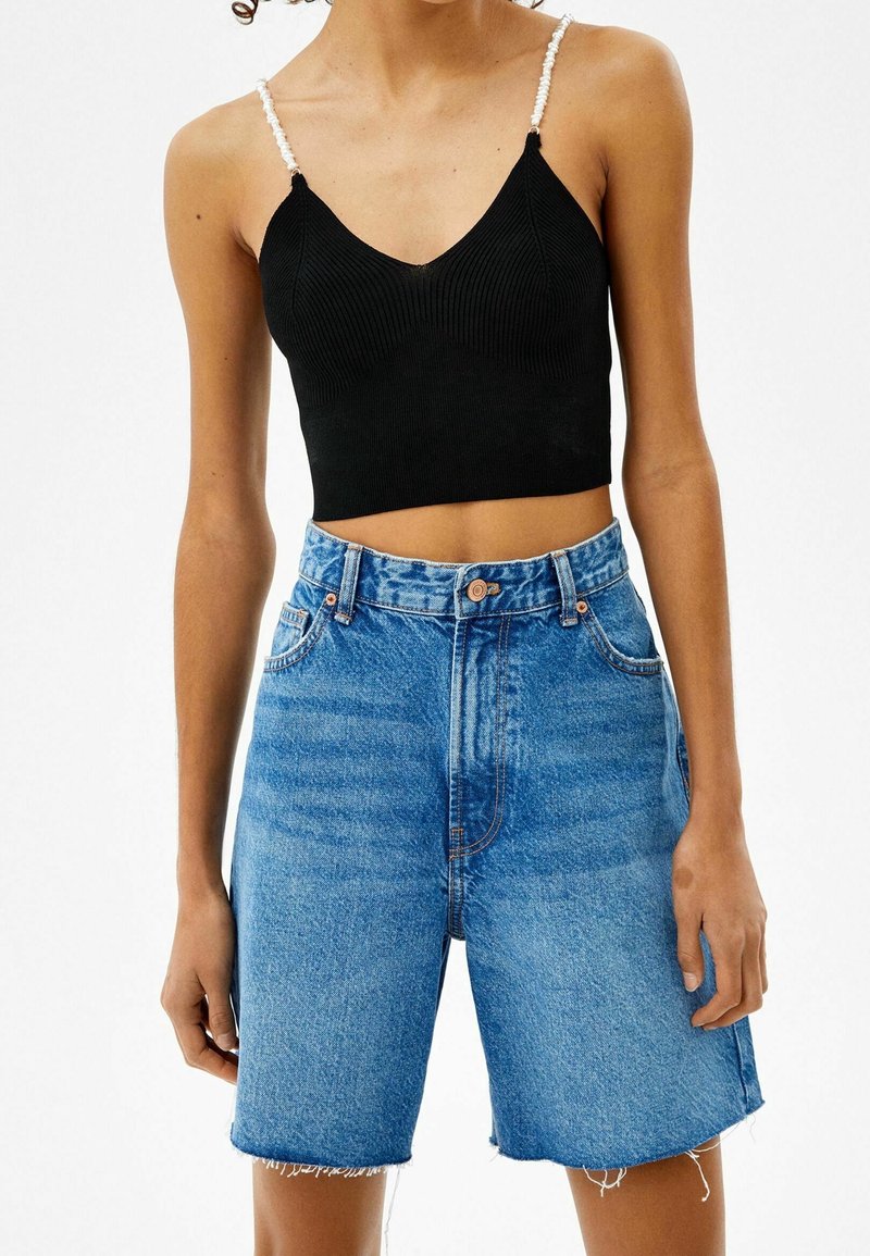 Svart ribbat crop top med justerbara vita pärlremmar, parat med högmidjade blå denimshorts med fransad nederkant och ljus tvätt.