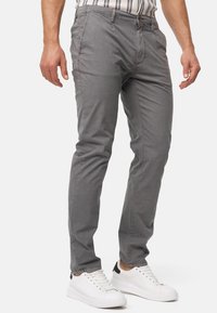 Grijze katoenen chino broek met een slanke pasvorm, steekzakken aan de voorkant en een knoopsluiting. Gecombineerd met witte sneakers. Vlakke voorkant, gladde textuur.