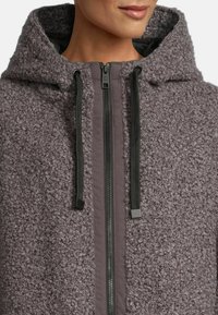 Gray, textured hooded jacket with a fuzzy exterior, featuring a contrasting smooth zipper closure and black drawstring accents.