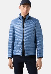 Light blue puffer jacket with a zip front, chevron quilted design, and high collar. Features black accents and a slim fit silhouette.