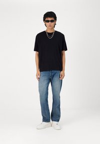 Black short-sleeve T-shirt, blue denim jeans, white sneakers, layered silver chains, and dark sunglasses. Plain and casual style.