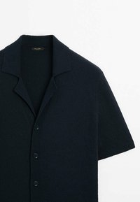 Short-sleeve, dark navy cardigan made of textured fabric. Features a classic collar and five button closure, with a smooth knit texture.
