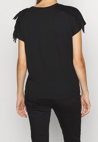 Svart t-shirt med korta ärmar, med fransdetalj på axlarna. Mjuk tyg, grundläggande rund halsringning, avslappnad passform.