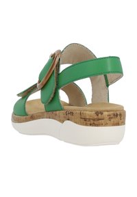 Sandale en cuir vert avec semelle en liège, semelle en caoutchouc blanche et un détail de boucle ronde proéminente. Design à brides croisées avec texture intérieure douce.