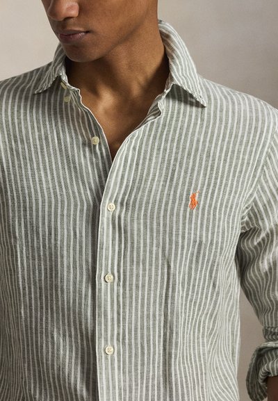 Férfi világosszürke és fehér, függőlegesen csíkos, gombolós ingben, mellkasán narancssárga hímzett logóval, feltűrt ujjakkal.