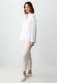 Camicia bianca in lino con colletto, caratterizzata da una vestibilità comoda; abbinata a pantaloni in lino beige chiaro a gamba affusolata e sneakers bianche.