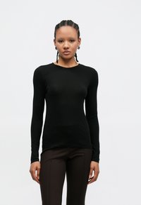 Camisola preta de manga comprida com decote redondo, silhueta ajustada e textura suave, combinada com calças castanhas. Design simples e minimalista.