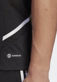 Camiseta atlética negra con una tela texturada, que presenta un logo y acentos blancos, y una franja blanca en contraste a lo largo de la costura lateral.