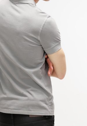 Polo en coton gris à manches courtes, coupe ajustée et texture lisse. Coutures visibles et détail subtil au col.