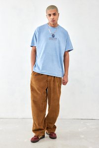 Light blue cotton t-shirt with graphic print; brown corduroy wide-leg pants; maroon shoes with yellow stripes; gold chain necklace.