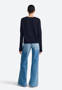 Granatowy sweter z prążkowanego dzianiny z długimi rękawami, w połączeniu z jasnoniebieskimi szerokimi jeansami o wyblakłym designie i postrzępionych krawędziach, widziane od tyłu.