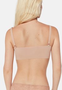 Sujetador sin costuras en tono nude con tirantes ajustables, que ofrece una silueta suave y un hardware mínimo, diseñado para mayor comodidad y soporte.
