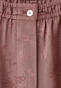 Tejido texturizado de color rosa-marrón con un patrón floral. Incluye un cierre de botón y detalle de cintura fruncida.