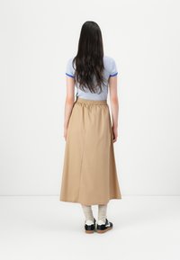 Larga falda marrón con cintura elástica, combinada con una camiseta a rayas gris y azul, y zapatos negros con detalles blancos.