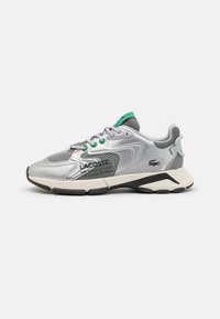 Silver athletic shoe with mesh and synthetic upper, green accents, padded collar, lace-up closure, and a thick black and white sole.