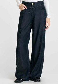 Wijdvallende donkere spijkerbroek met knoopsluiting en trekkoord, met voorzakken en een zachte textuur.