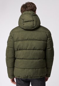 Grøn pufferjakke med en tekstureret overflade, der har horisontale syninger, hætte og en afslappet pasform. Bagsiden viser det quiltede design.