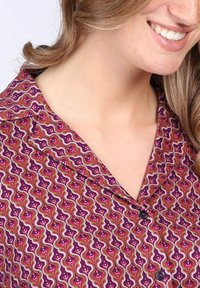 Purple patterned blouse featuring a wavy design with pink and green accents, a collared neckline, and black buttons.